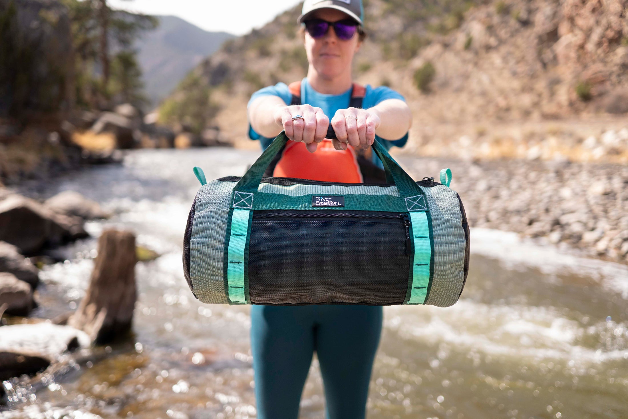 Person holding a green and black duffel bag by a river